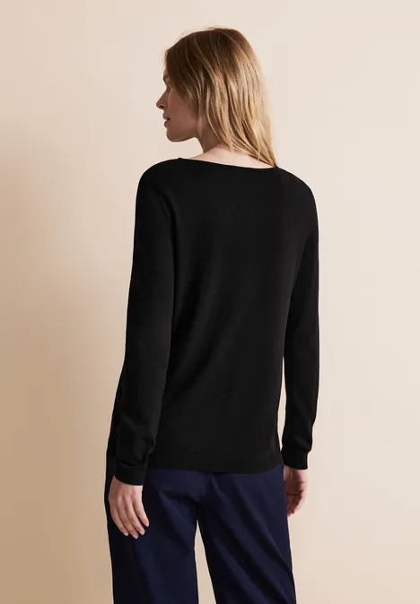 Frau mit schwarzem Pullover, von hinten zu sehen, steht vor beigem Hintergrund.
